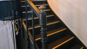 Un escalier avec des balustrades noires et des bordures jaunes, menant à un palier où se trouve un pot de fleurs.