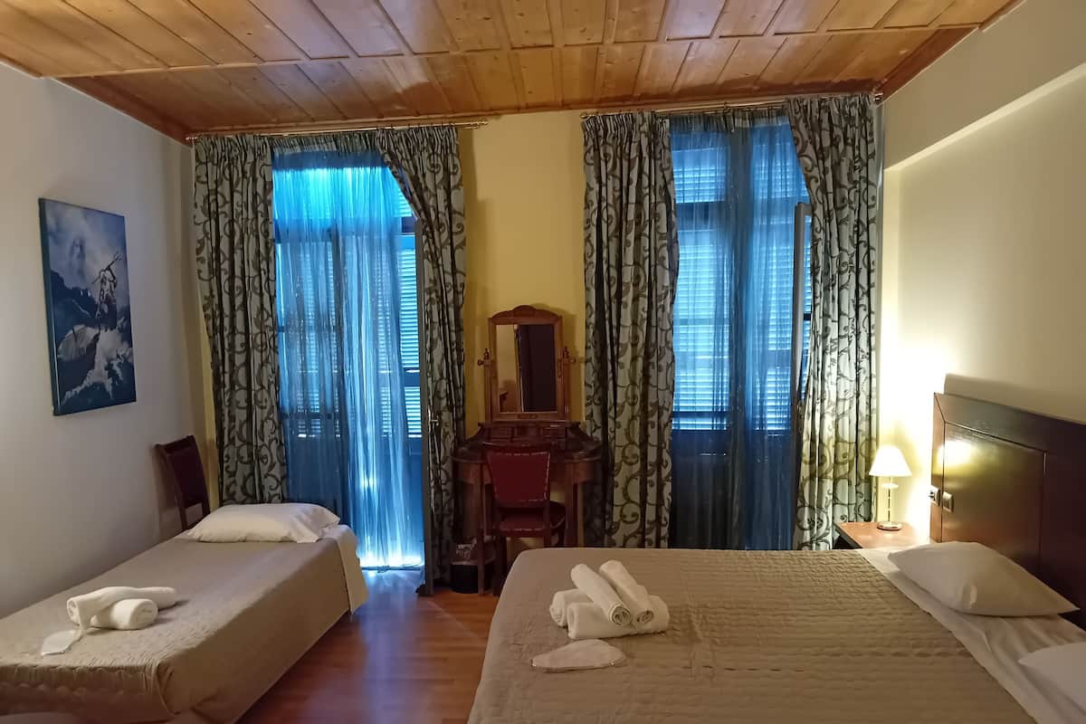 A hotel room with two beds, wooden ceiling, a painting on the wall, and patterned curtains.