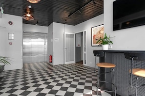 A lobby with a checkered floor, a reception desk with stools, a potted plant, and a fire extinguisher. - Swan Stylish Double Studio (Reykjavík)