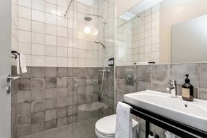 A modern bathroom with a glass-enclosed shower, a white toilet, and a sink with a soap dispenser. - Swan Studio Basement in Downtown (Reykjavík)