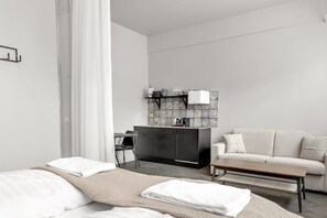 A modern hotel room with a bed, a sofa, a small table, a desk, and a kitchenette. - Swan Studio Basement in Downtown (Reykjavík)