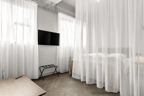 A modern bedroom with a bed, a TV mounted on the wall, and sheer curtains. - Swan Basement Studio in Downtown (Reykjavík)
