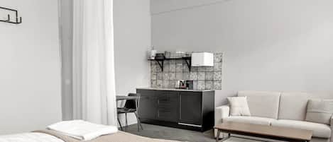 A modern hotel room with a bed, a sofa, a small table, a desk, and a kitchenette.