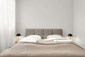 A neatly made bed with a grey headboard, white linens, and two black bedside lamps. - Swan Studio Basement in Downtown (Reykjavík)