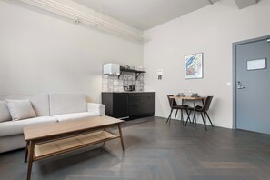 A modern living room with a sofa, a coffee table, a dining area with chairs, a kitchen with a microwave, and a door with a sign.