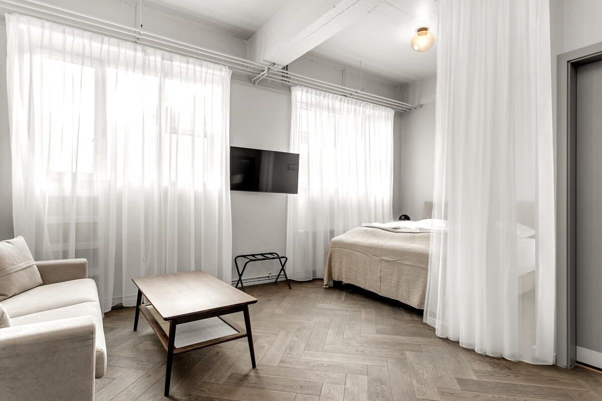 A modern, minimalist bedroom with a bed, a TV mounted on the wall, and a small table.