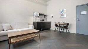 A modern living room with a sofa, a coffee table, a dining area with chairs, a kitchen with a microwave, and a door with a sign. - Swan Basement Studio in Downtown (Reykjavík)