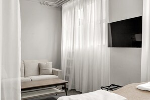 A modern hotel room with a sofa, a small table, a TV mounted on the wall, and sheer curtains. - Swan Basement Studio in Downtown (Reykjavík)