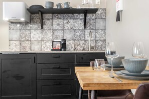 Une cuisine moderne avec un mur recouvert de carreaux, une machine à café et une table à manger en bois, agrémentée de verres.