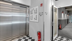 A hallway with a fire extinguisher, a fire alarm, and a door leading to another room. - Swan Basement Studio in Downtown (Reykjavík)