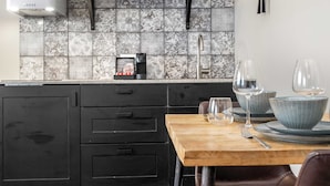 Una cocina moderna con salpicadero de azulejos, una cafetera y una mesa de comedor de madera con cristalería.