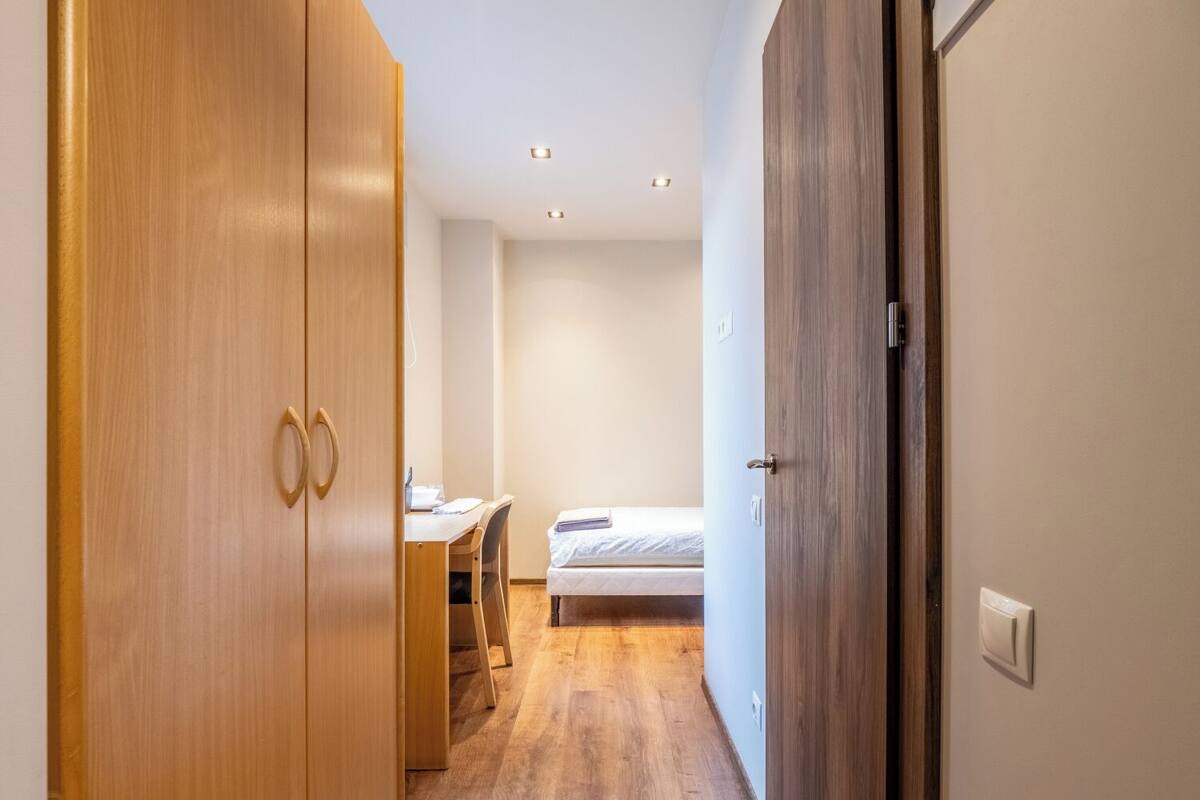 Un couloir mène à une chambre qui comprend un bureau avec une chaise, une armoire en bois et un lit.