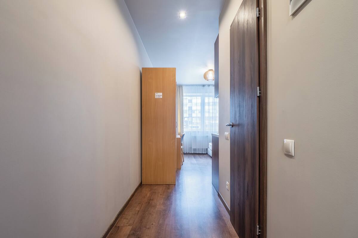 Un couloir avec un plancher en bois, une porte en bois et un interrupteur sur le mur.