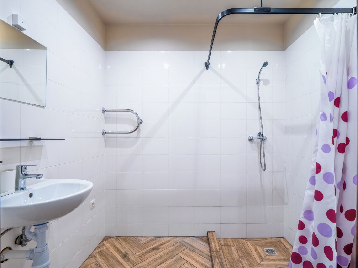 Un baño con lavamanos blanco, un espejo, una ducha con cabezal de ducha manual y una cortina de ducha con lunares.