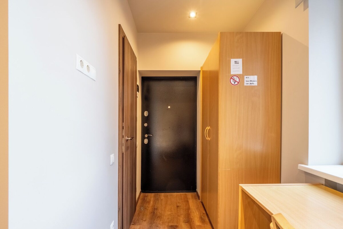 A narrow hallway with wooden flooring, a black door at the end, and a wooden cabinet on the right.
