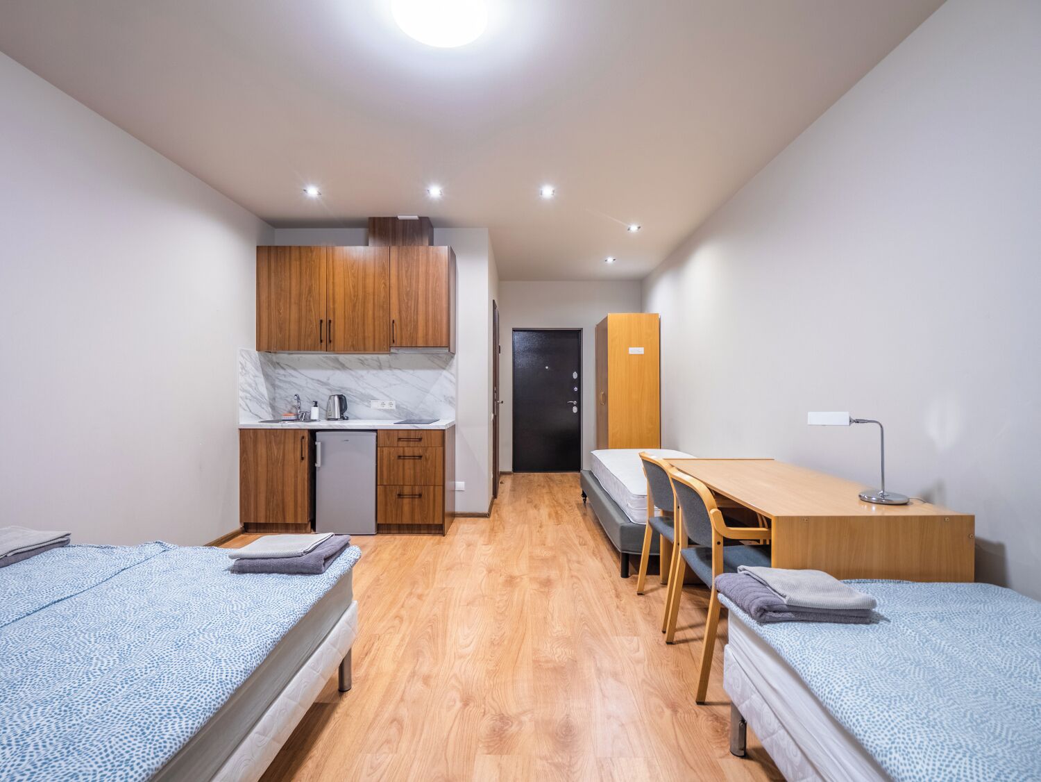 Una habitación pequeña con dos camas, un kitchenette reducido, un escritorio y una silla.