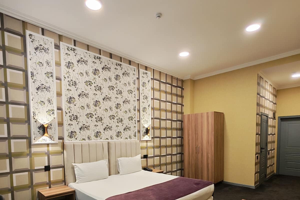 A hotel room with a bed, bedside tables, a desk, a wardrobe, and a partition with floral wallpaper.