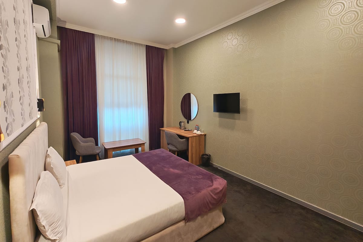 A hotel room with a bed, a desk, a chair, a TV, and a window with curtains.