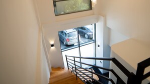 A staircase with wooden steps and black railings, leading to a room with a large window and a chandelier. - Will Hotel (Baku)