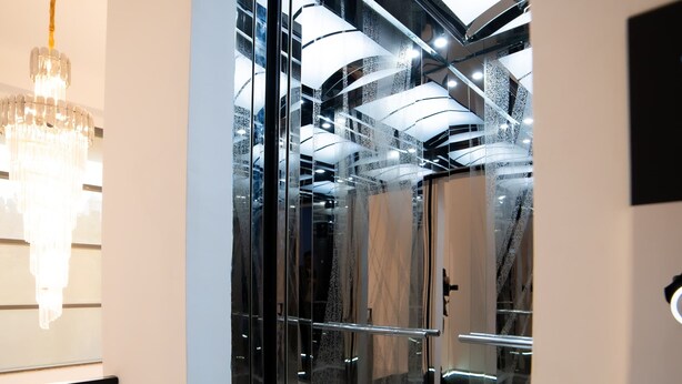 A modern elevator with glass doors, a chandelier, and a view of the building's interior. - Will Hotel (Baku)