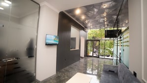 A modern hotel lobby with a glass wall, a flat-screen TV, a sofa, and a staircase leading to an outdoor area. - Will Hotel (Baku)