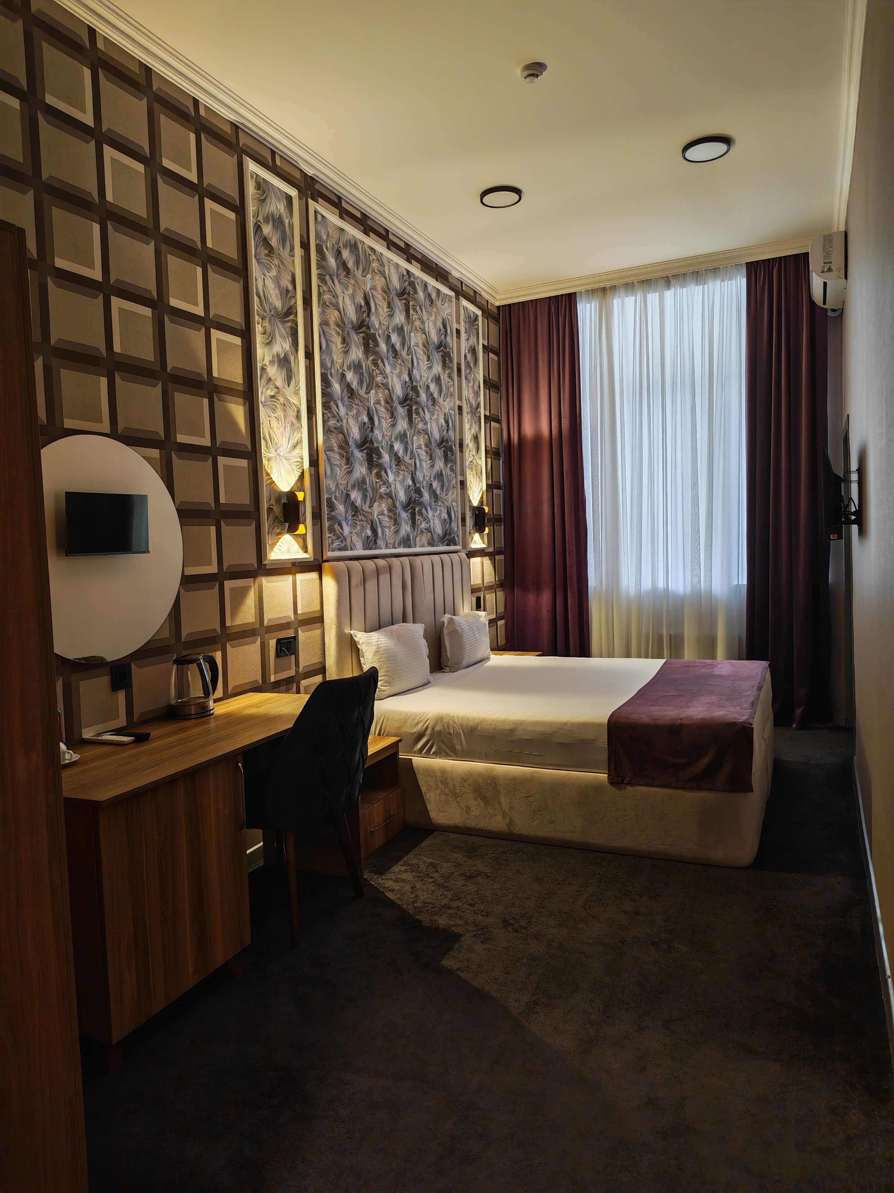 Hotelkamer met een bed, bureau, stoel en een groot raam met gordijnen.