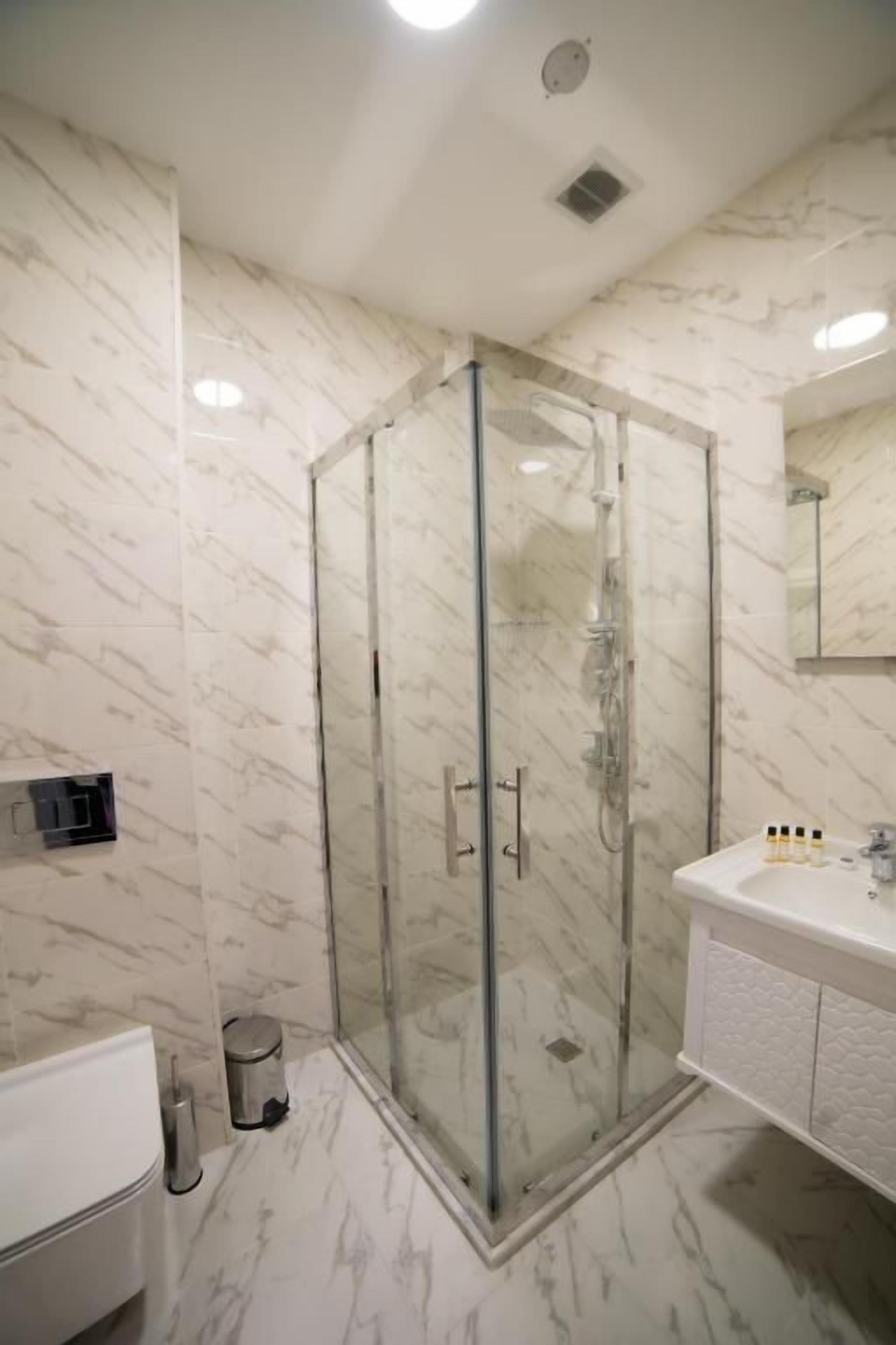 A modern bathroom with a glass-enclosed shower, a white sink with toiletries, and a marble-patterned wall.