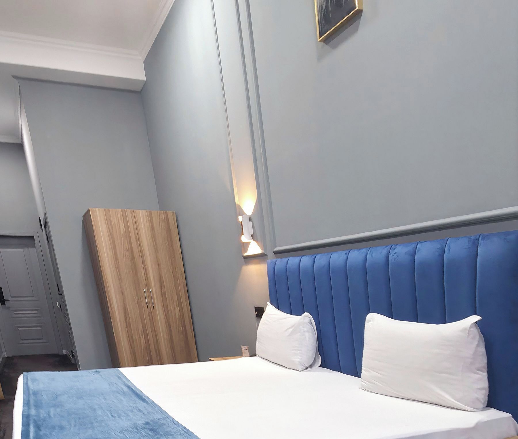 A bedroom with a bed, a wooden wardrobe, and a wall-mounted light fixture.