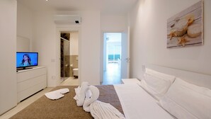A modern hotel room with a large bed, a TV, a bathroom, and a view of the sea.