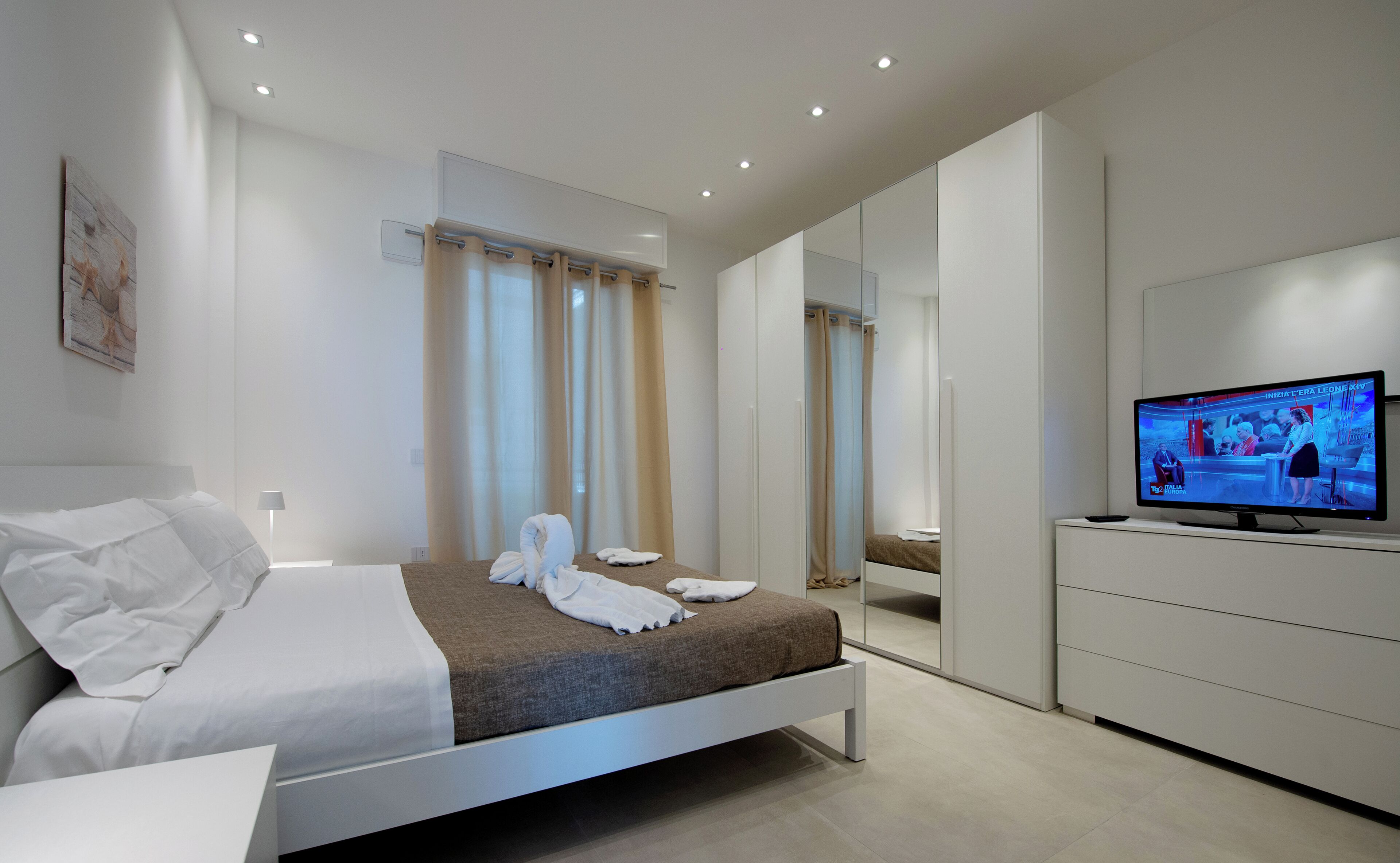Una camera d'albergo moderna con un letto, una televisione e uno specchio grande.