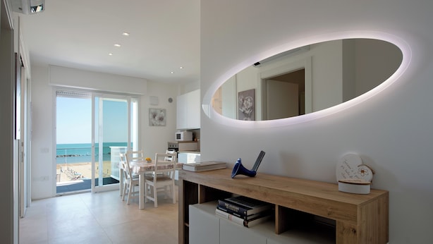 A modern living room with a wooden console table, a large oval mirror, and a view of the beach through glass doors.
