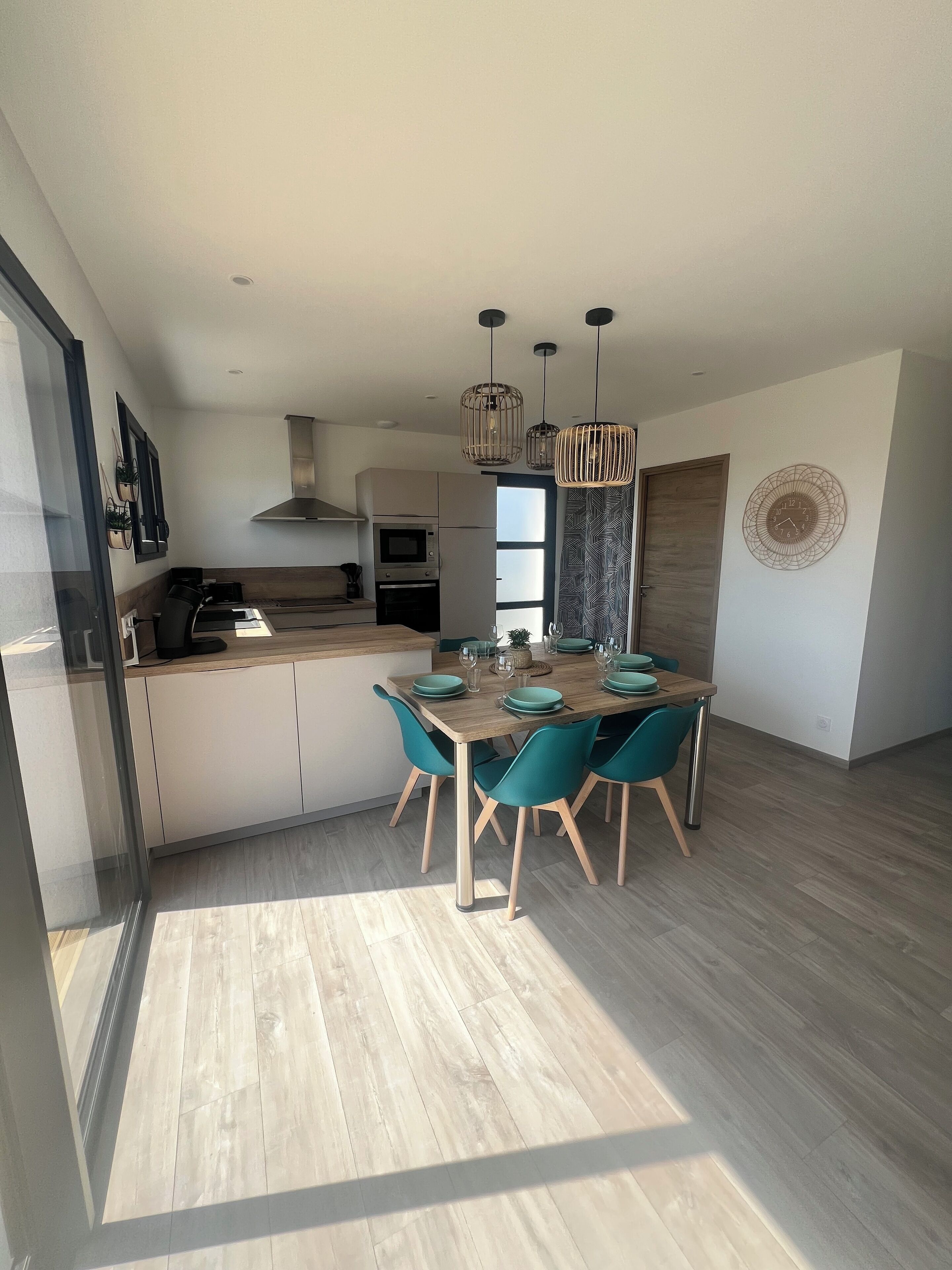 Una cocina moderna con una isla central, electrodomésticos integrados y sillas color turquesa alrededor de una mesa de comedor de madera.