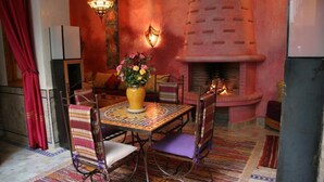 A cozy dining area with a table set for two, surrounded by patterned chairs, a vase of flowers, and a fireplace. - RIAD KENZO (Marrakech)