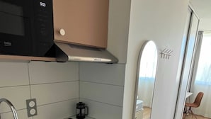 A modern kitchen with a sink, stove, and microwave. There is a small island with a coffee maker and a mirror on the wall. - Comfort Studio in a Premium Residence- Sport/cinema (Huningue)
