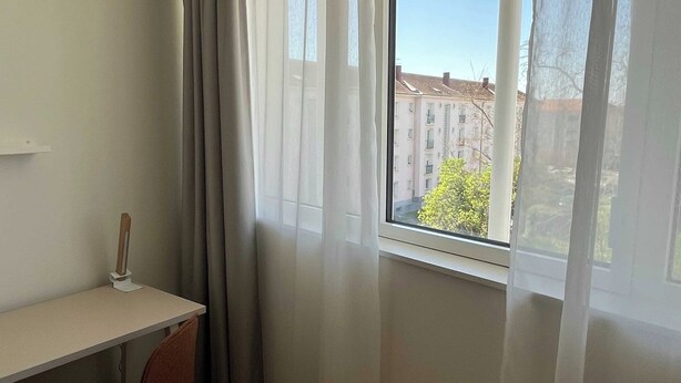 A room with a desk, chair, and a large window with curtains. - Comfort Studio in a Premium Residence- Sport/cinema (Huningue)