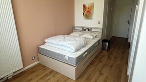 A bedroom with a bed, a radiator, a wall-mounted picture, and a door. - Comfort Studio in a Premium Residence- Sport/cinema (Huningue)