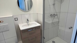 A modern bathroom with a sink, mirror, and shower. - Comfort Studio in a Premium Residence- Sport/cinema (Huningue)