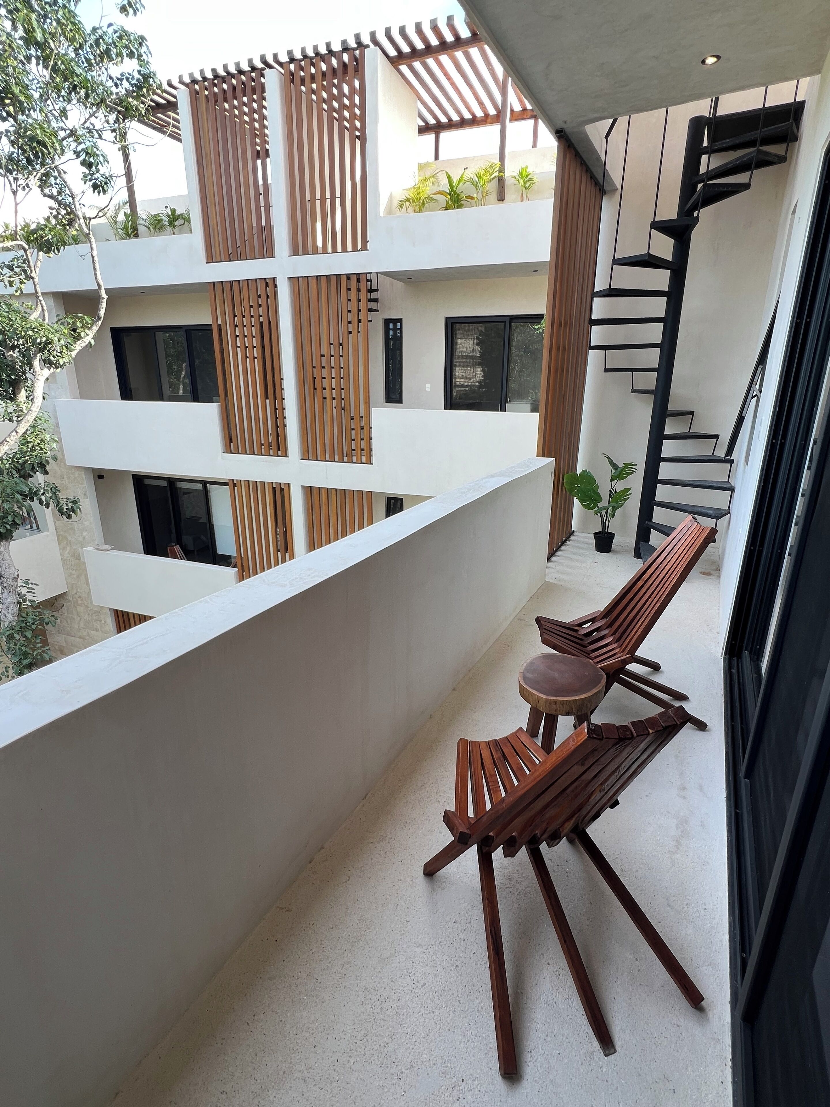 A modern outdoor balcony with wooden furniture and a spiral staircase.