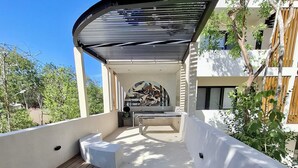 Un'area esterna riparata con un pavimento in legno, una zona relax e vista su un edificio moderno con facciata bianca e elementi in legno.