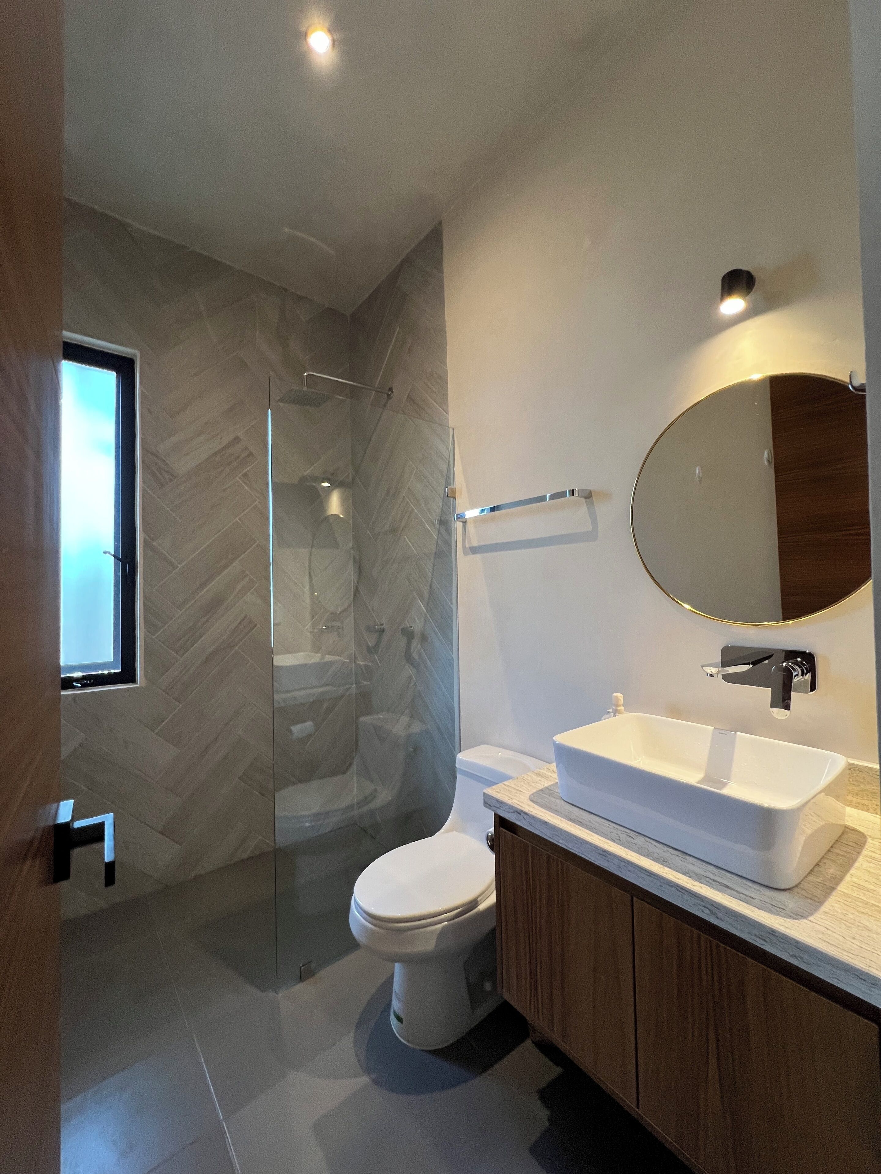 A modern bathroom with a glass shower enclosure, a white toilet, and a vanity with a large mirror.