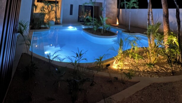 Un edificio moderno con piscina, circondato da alberi e piante.
