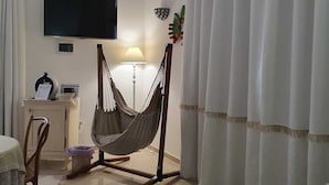 Una sala de estar con una silla hamaca, un televisor de pantalla plana, una lámpara y una mesita con una cesta.