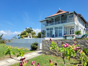 A two-story house with a balcony, a stone wall, and a pathway leading to the entrance. - Stara's Escape a Coastal Haven - Entire home in Scarborough, Tobago (Scarborough)