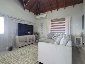 Una sala de estar con televisor, sofá y cojines decorativos.