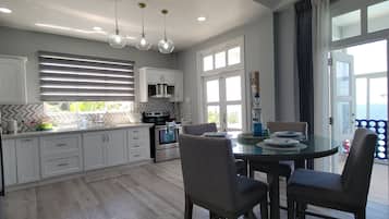 A modern kitchen with white cabinets, a dining table with four chairs, and a view of the sea through large windows.