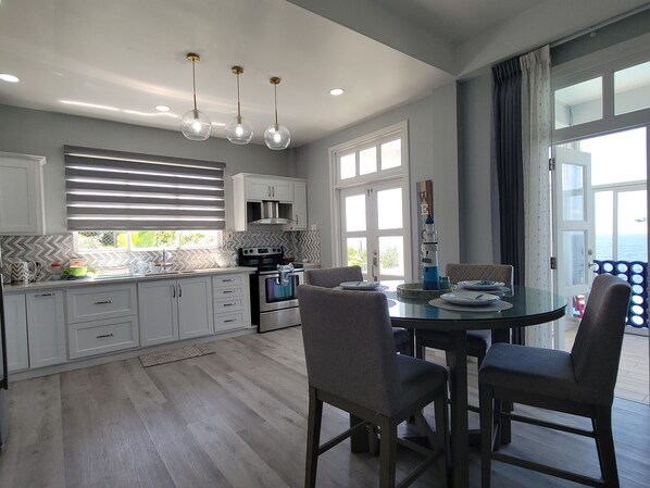 Una cocina moderna con armarios blancos, una mesa de comedor con cuatro sillas y vistas al mar a través de amplios ventanales.