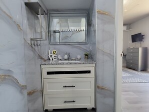 Un baño con tocador de mármol, un espejo y un lavamanos.