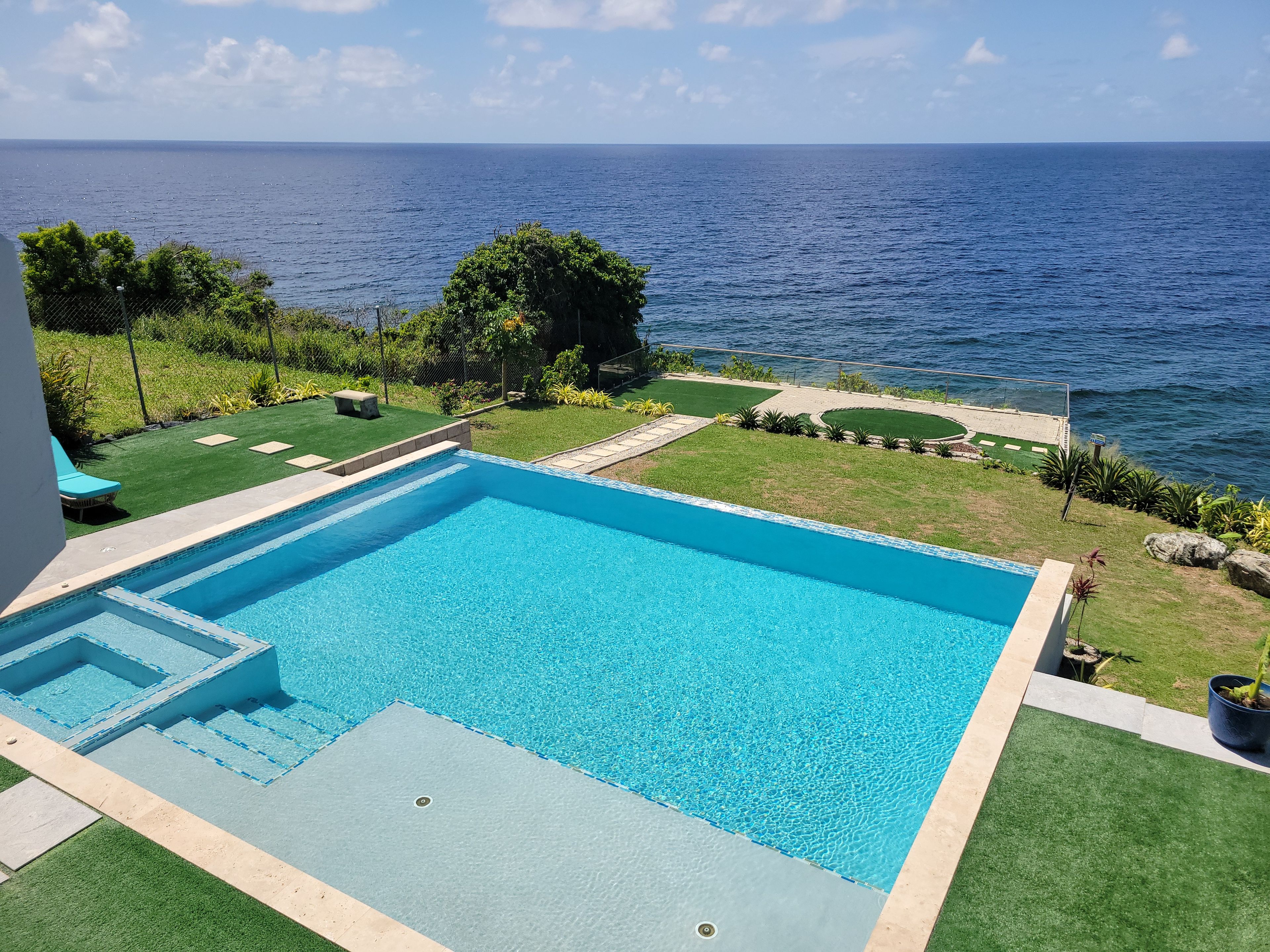 A rectangular swimming pool with a clear blue water feature, surrounded by a well-maintained lawn and a view of the ocean.