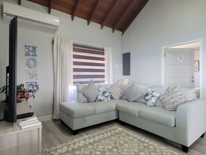 A living room with a light-colored sofa, a patterned rug, and a television on a stand. - Stara's Escape a Coastal Haven - Entire home in Scarborough, Tobago (Scarborough)