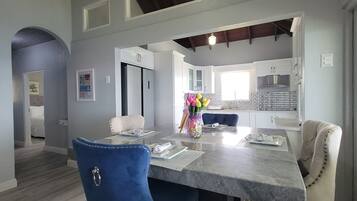 A modern kitchen with white cabinets, a marble countertop, and a dining area with a blue chair and a vase of flowers.